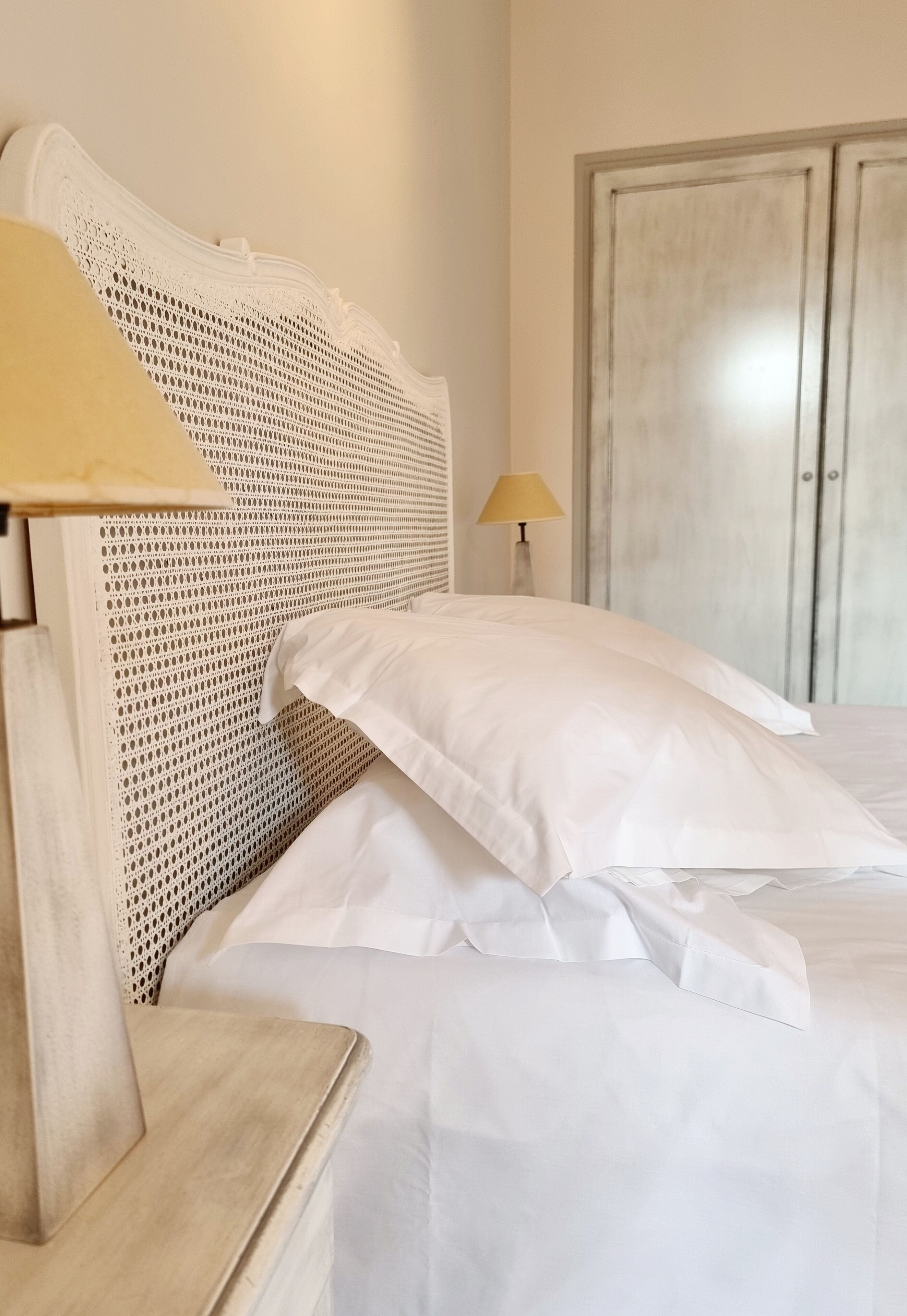 Una cama bien tendida con sábanas blancas y un cabecero tejido.