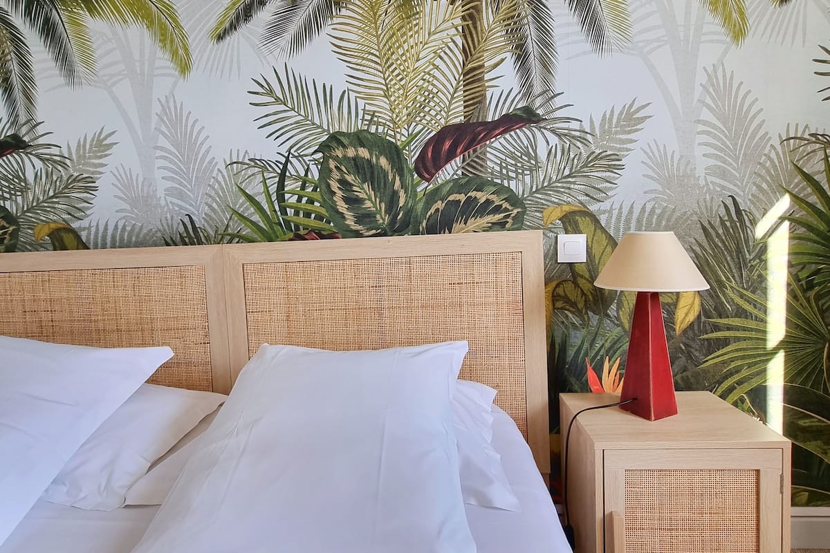 A bed with white linens, a wooden headboard, and a nightstand with a red lamp.