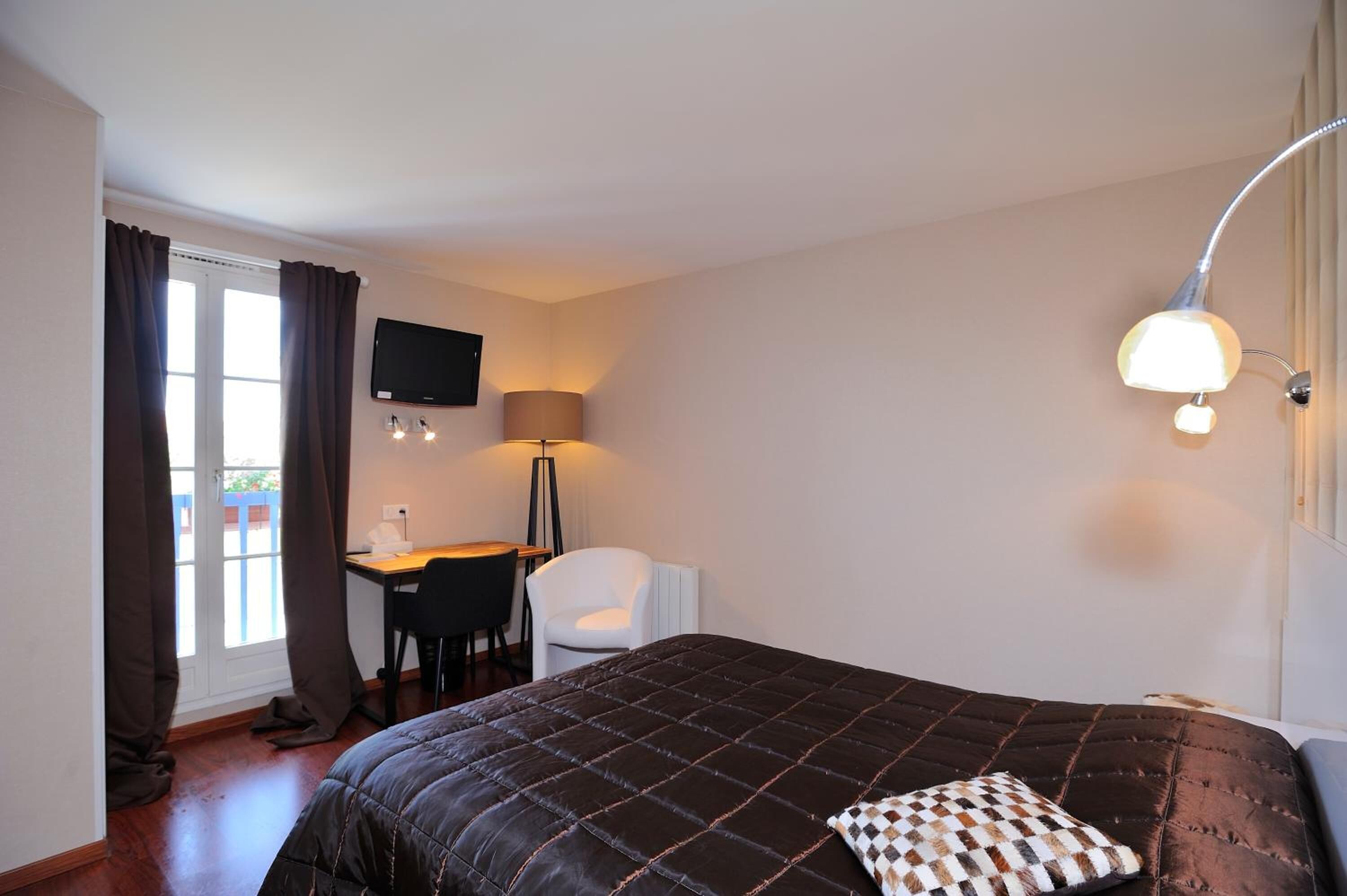 A bedroom with a bed, a desk, a chair, a TV, and a lamp.