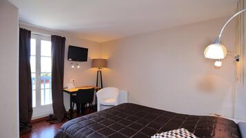 A bedroom with a bed, a desk, a chair, a TV, and a lamp.