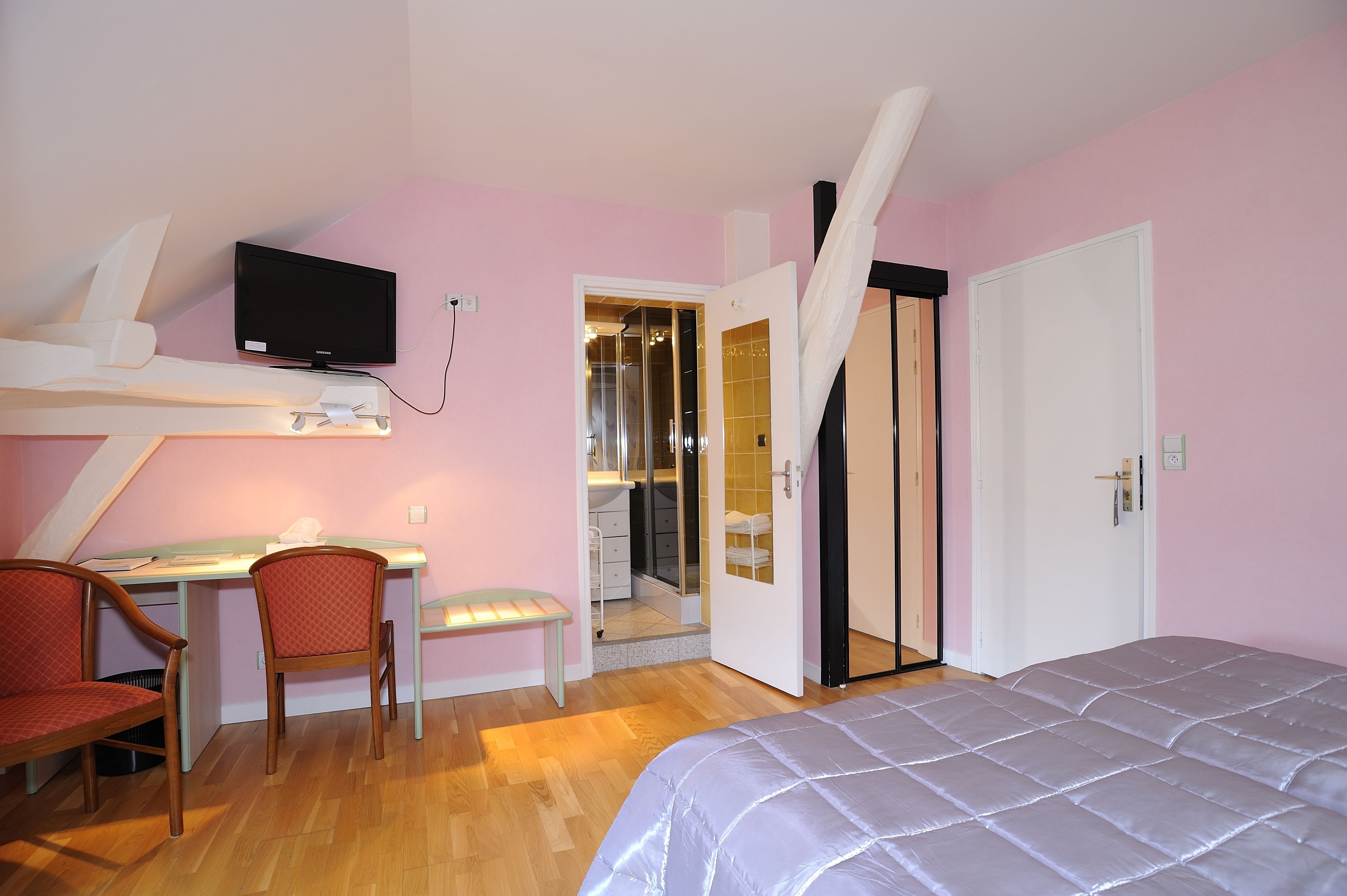 Un dormitorio con una cama, un escritorio con silla, un televisor y una puerta que da a un baño.