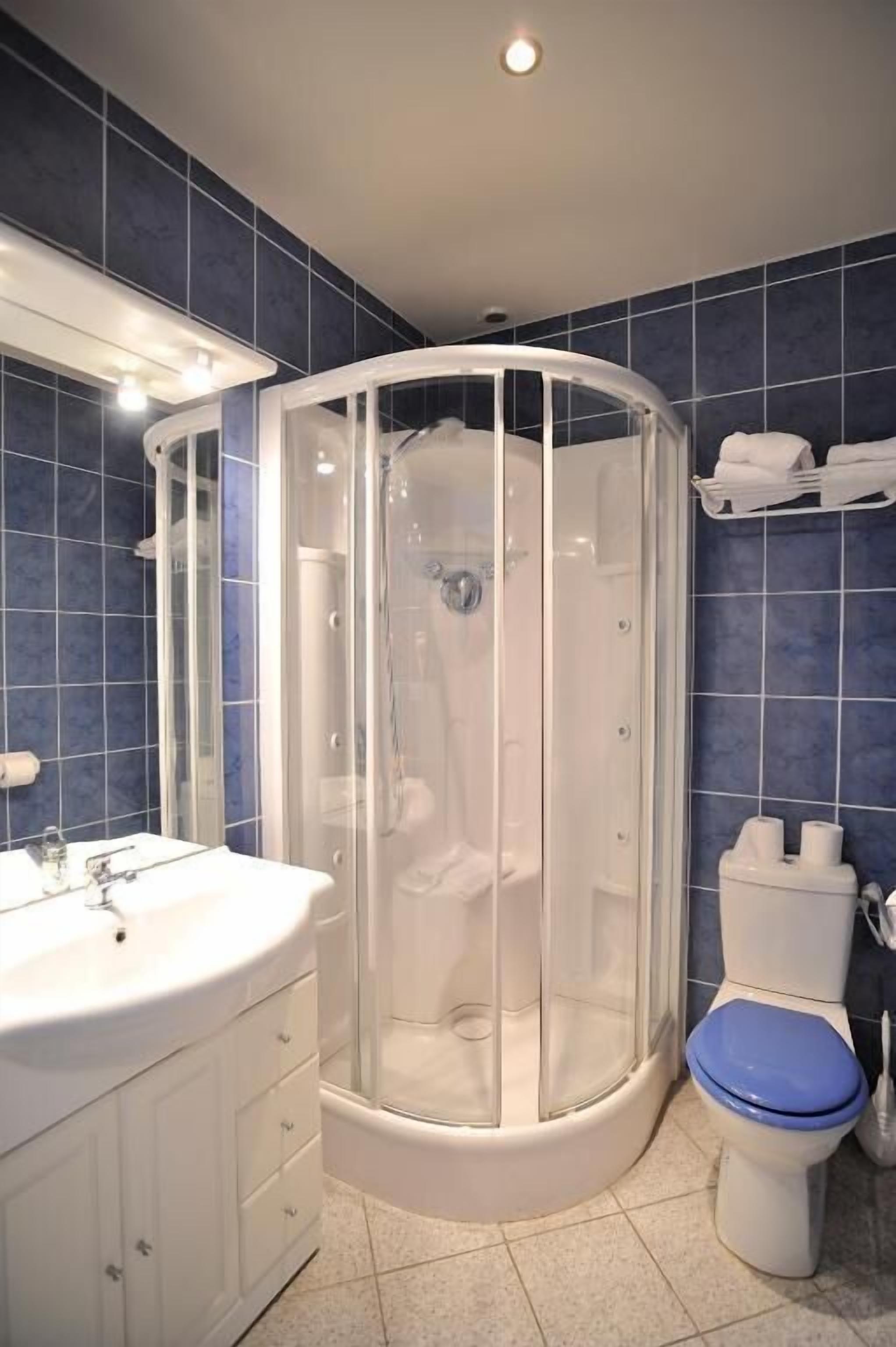 Un baño con ducha de vidrio, lavamanos blanco y un inodoro con el asiento azul.