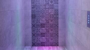 Um chuveiro estreito revestido com azulejos, parede estampada e luminária circular no teto.