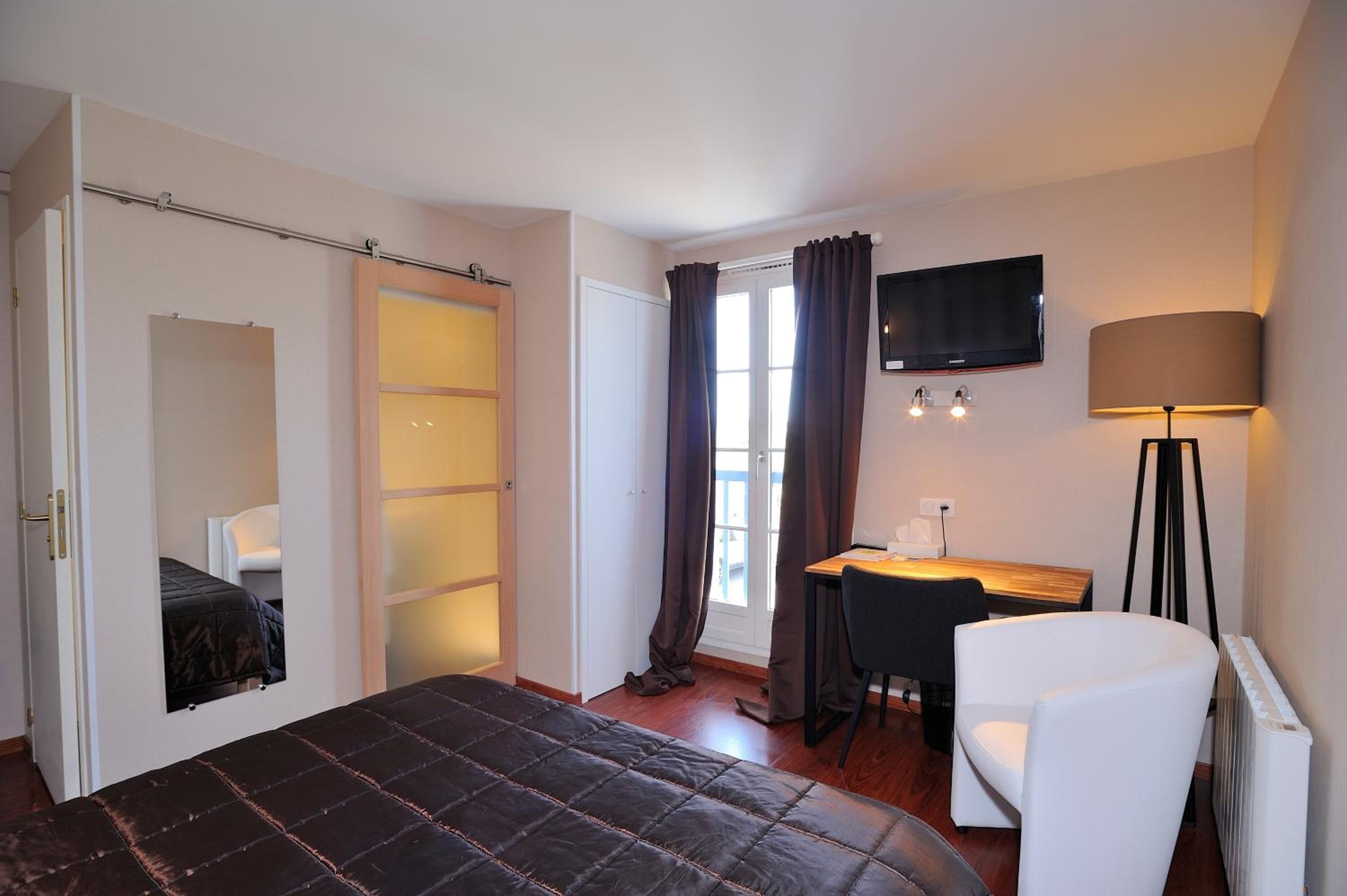A bedroom with a bed, a desk, a chair, a TV, and a lamp.