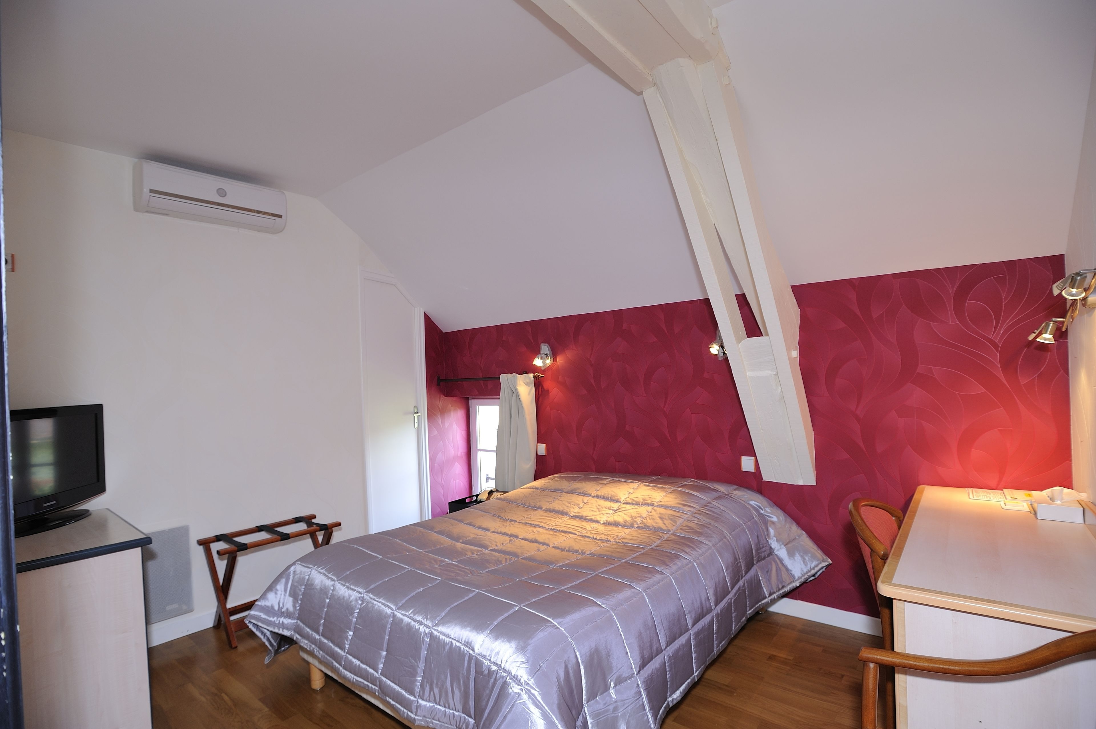 A bedroom with a bed, a desk, a chair, a television, and an air conditioning unit.