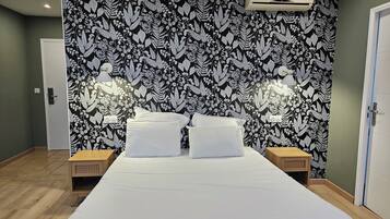 A bedroom with a large bed, two bedside tables, a wall-mounted air conditioner, and a floral-patterned wallpaper.