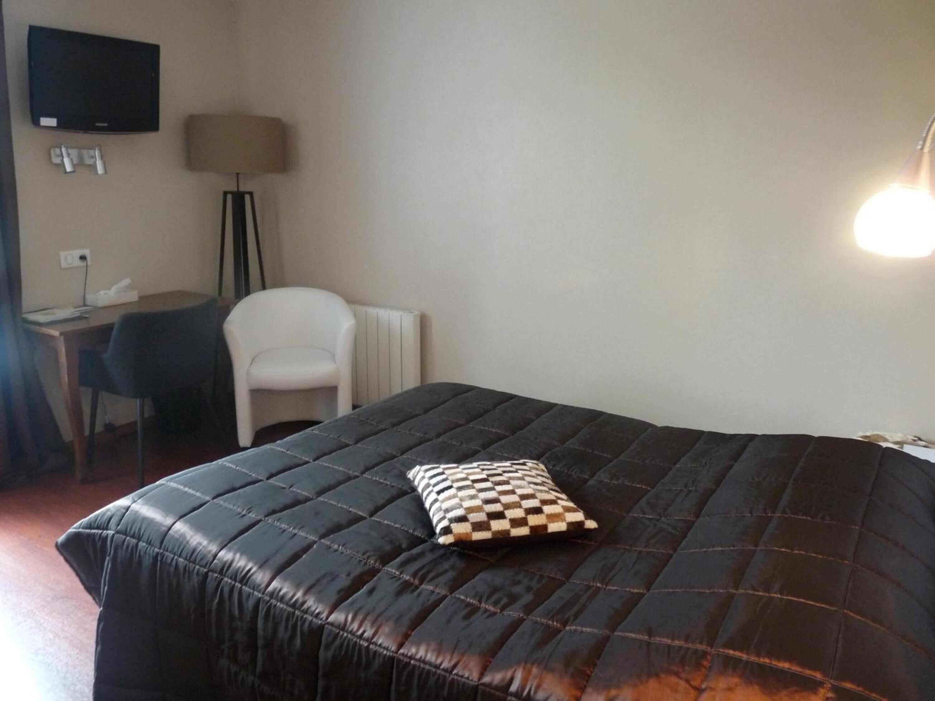 Una habitación con una cama, un escritorio, una silla y un televisor en la pared.