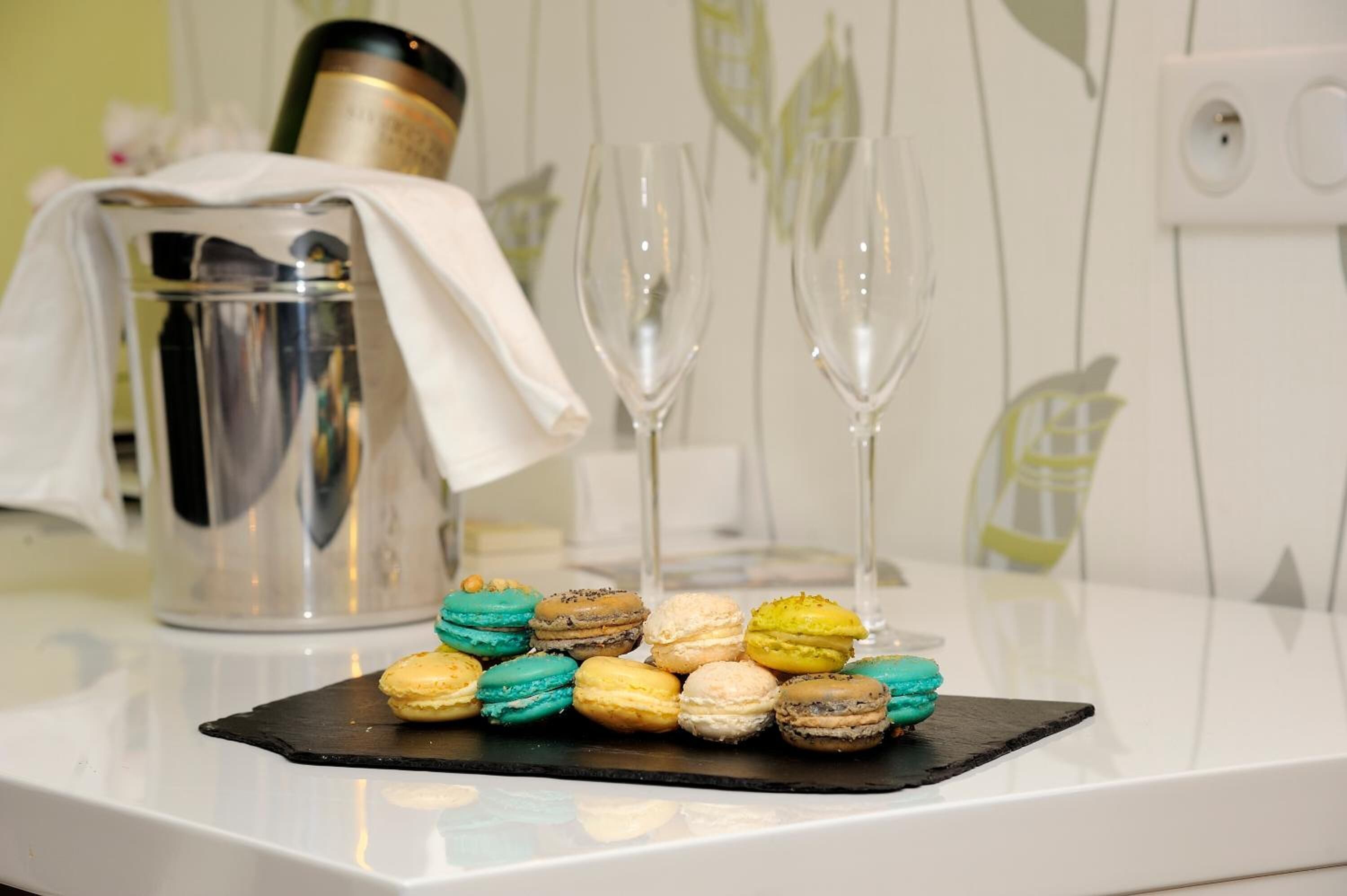 Un bancone cucina con un vassoio di macaron colorati, una macchina per il caffè e due bicchieri da vino vuoti.