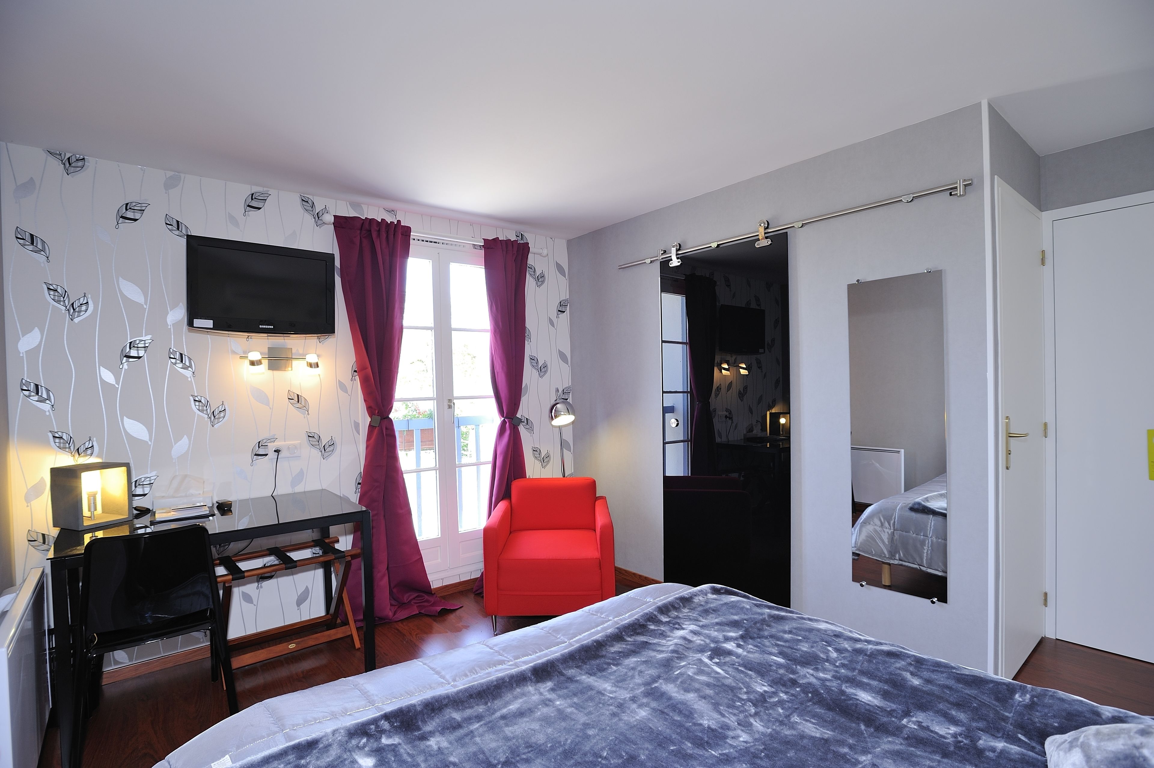 Een slaapkamer met een bed, een bureau, een stoel, een televisie en een deur naar een andere kamer.