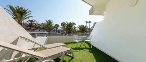 Una terraza en la azotea con césped artificial, sillones blancos y una pared blanca.