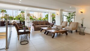 Amplia sala de estar con sofá, sillones y mesas de centro, con ventanas amplias y plantas de interior.