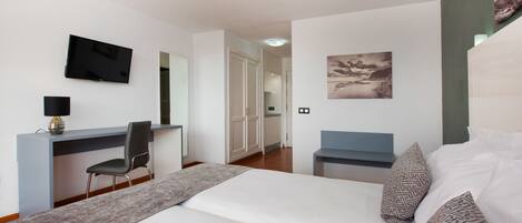 Un dormitorio con cama, escritorio, silla, televisor y un cuadro en la pared.
