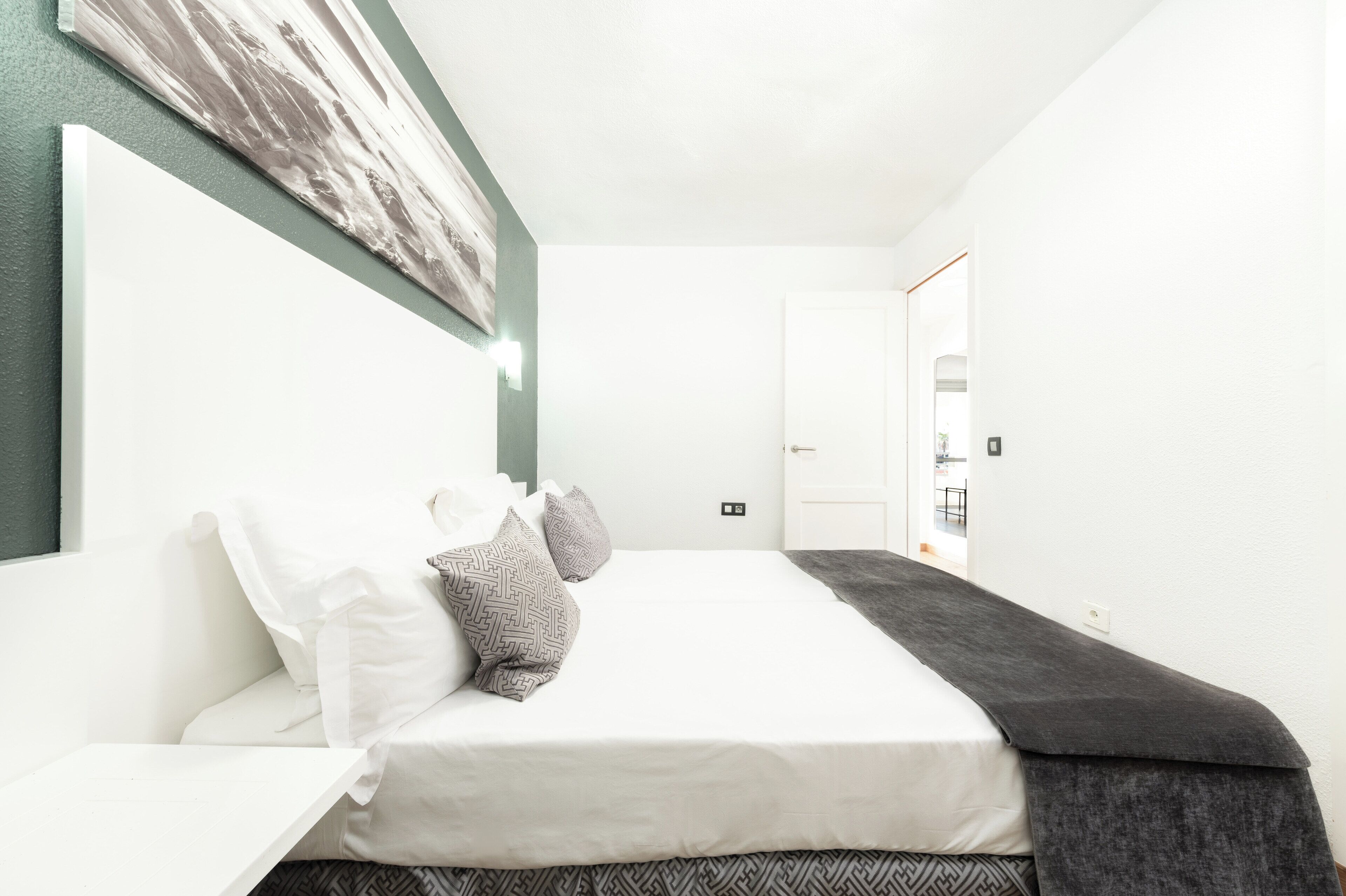Una habitación de hotel moderna con una cama grande, paredes blancas y un cuadro sobre la cama.