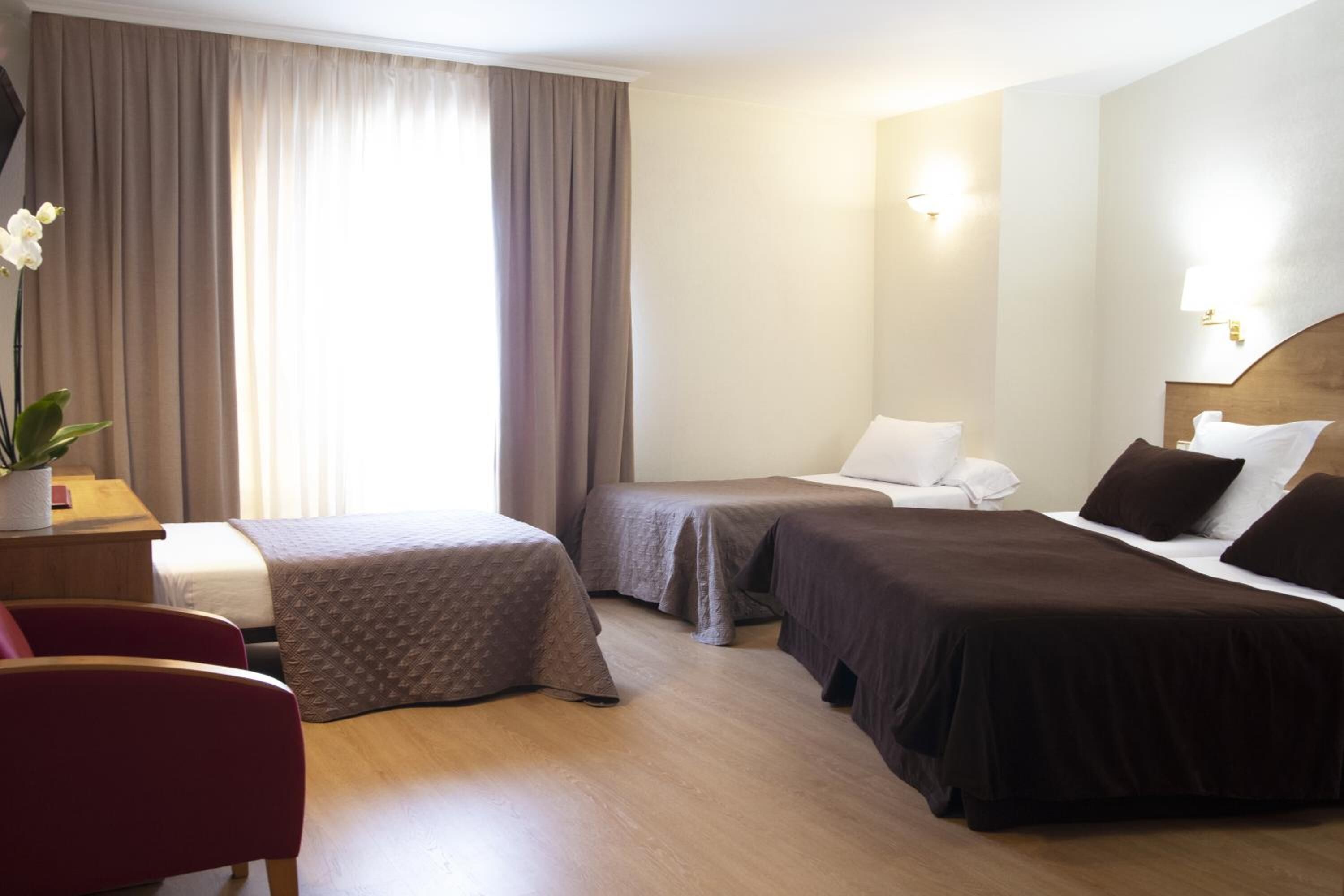 Une chambre d’hôtel avec deux lits simples, un bureau avec une chaise et une grande fenêtre avec des rideaux.