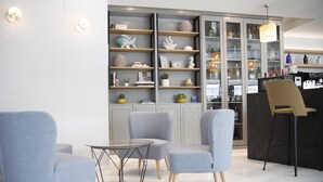 A modern interior with grey upholstered chairs, a glass table, and a bar area with shelves and bottles.