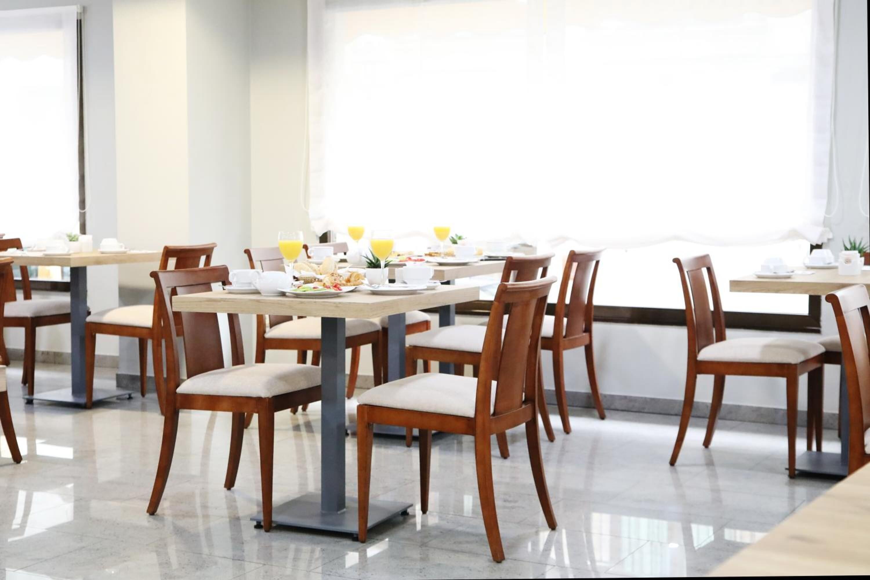 A dining area with multiple tables and chairs, arranged in a spacious layout with large windows providing natural light.