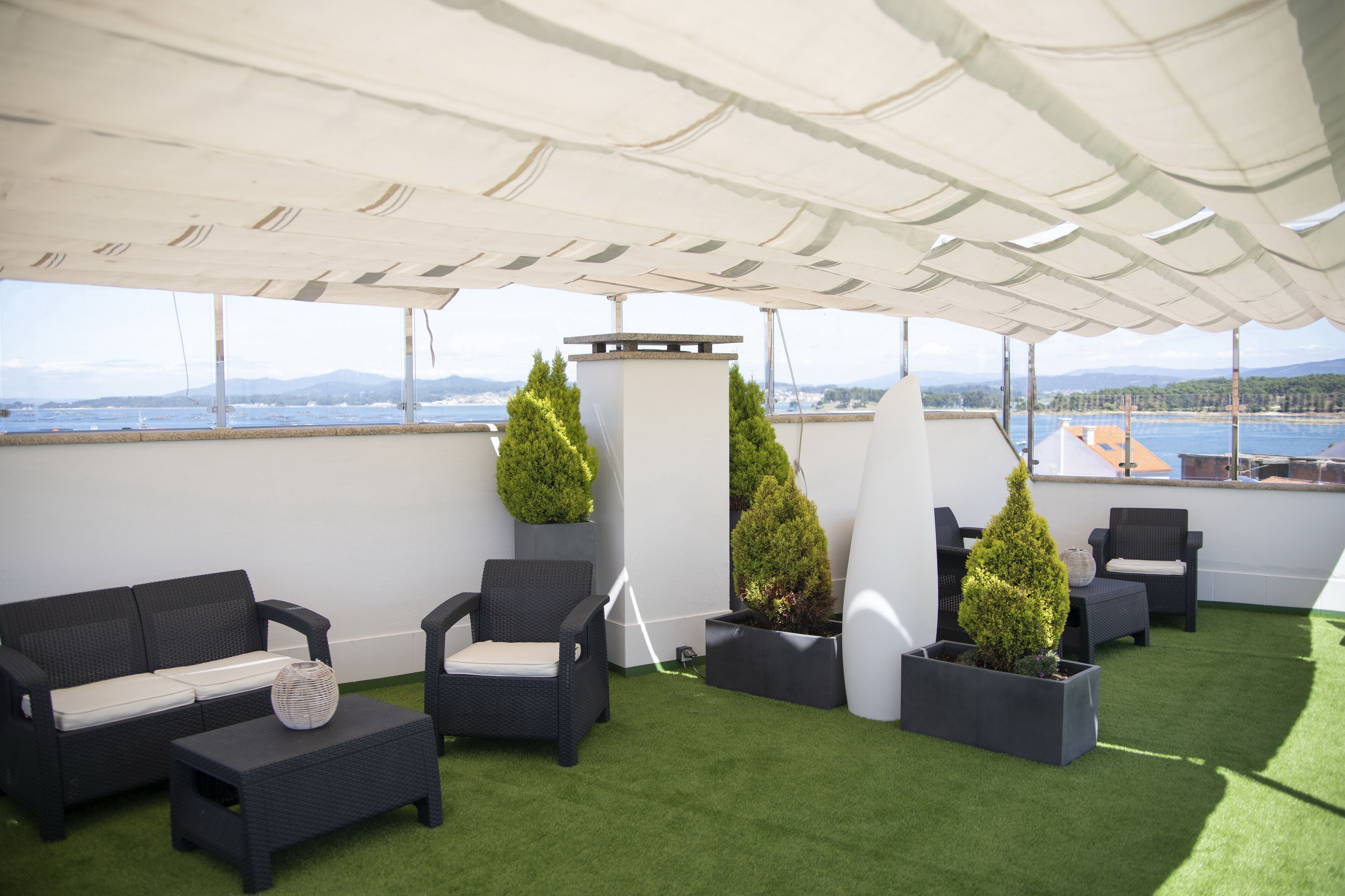 A rooftop terrace with a white canopy, black wicker furniture, and green artificial grass.