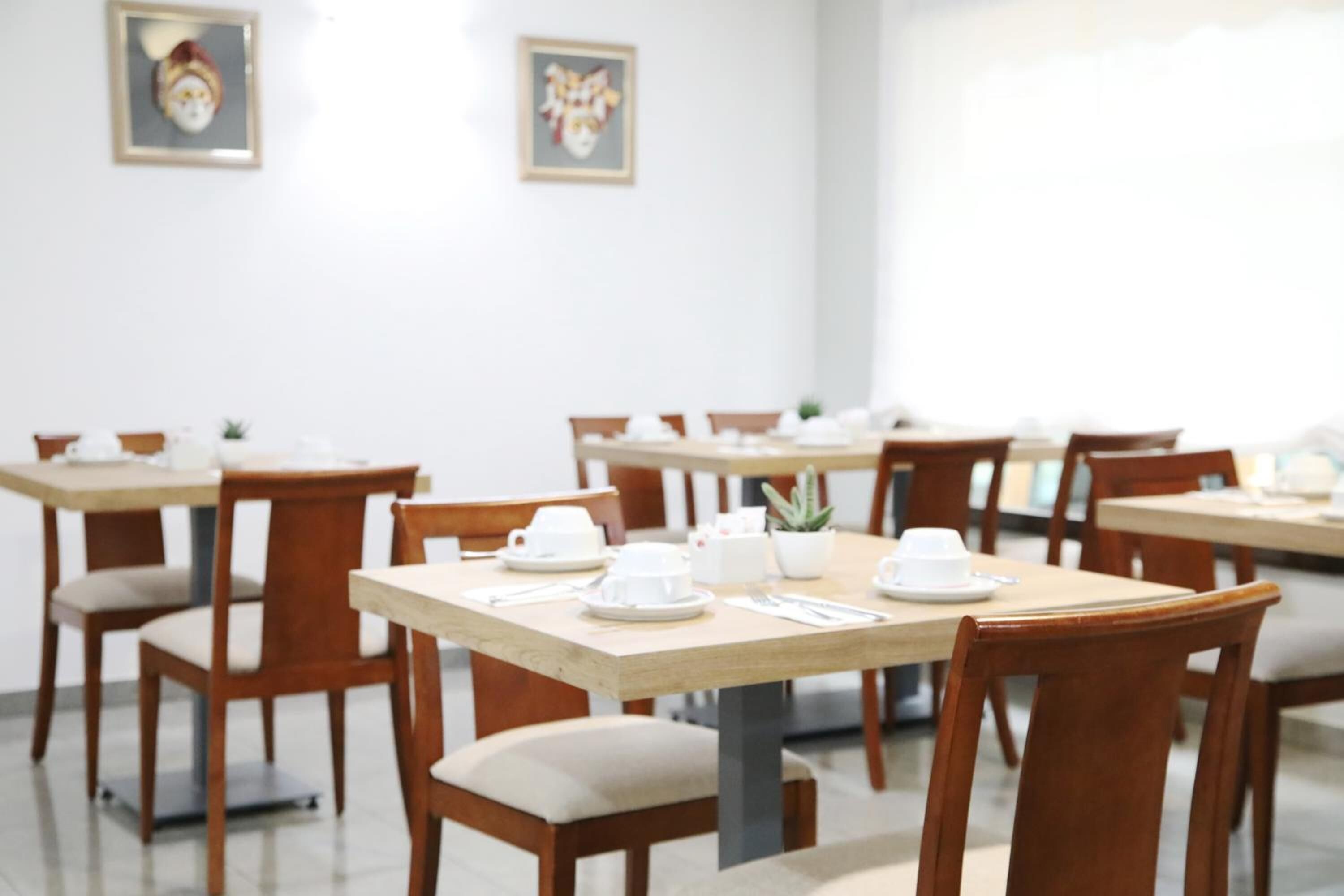 Un comedor con varias mesas y sillas, cada conjunto con vajilla blanca y una pequeña planta en maceta.