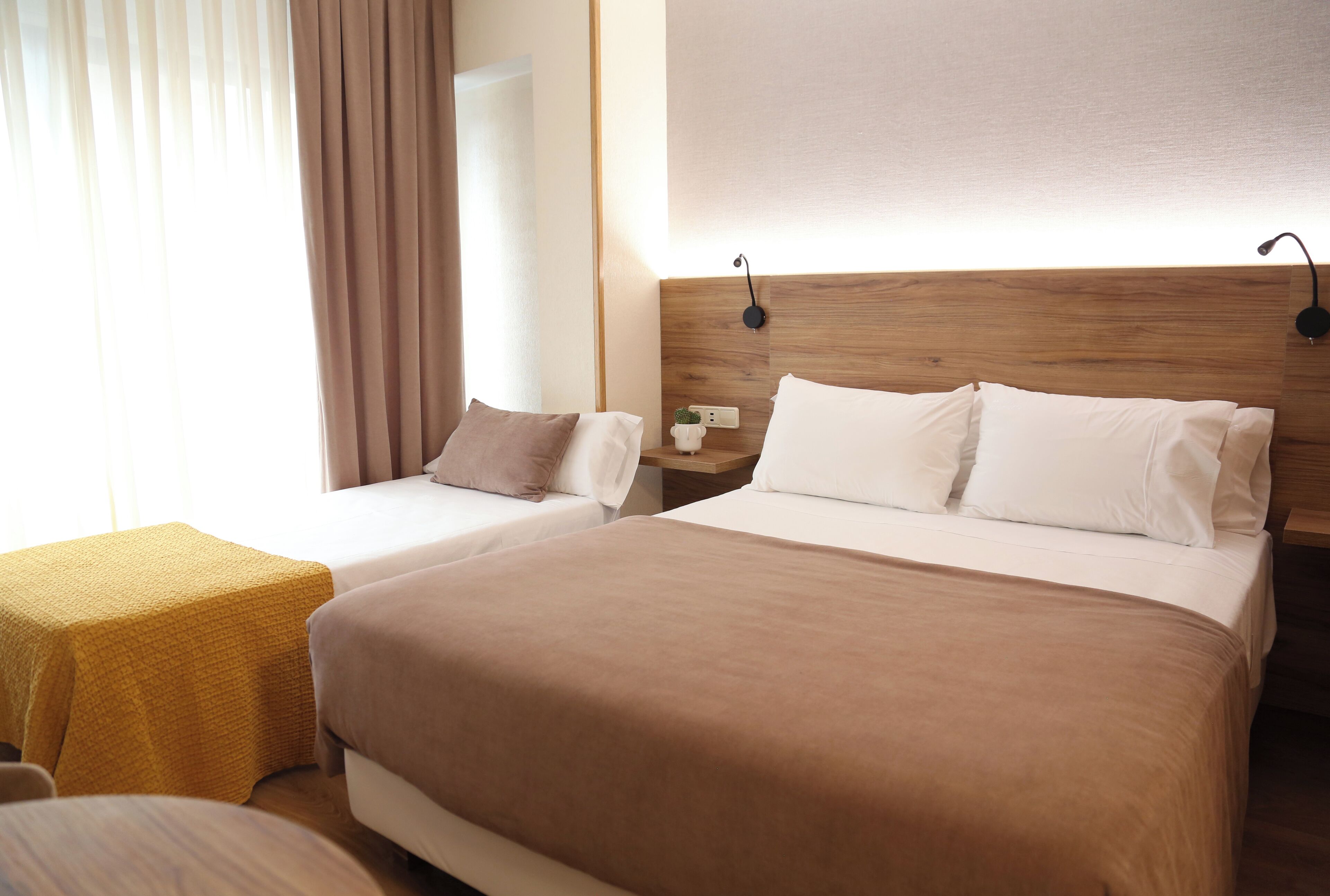 Ein Hotelzimmer mit zwei Betten, einem hölzernen Kopfteil, einem Nachttisch und einem kleinen Tisch mit gelber Tischdecke.