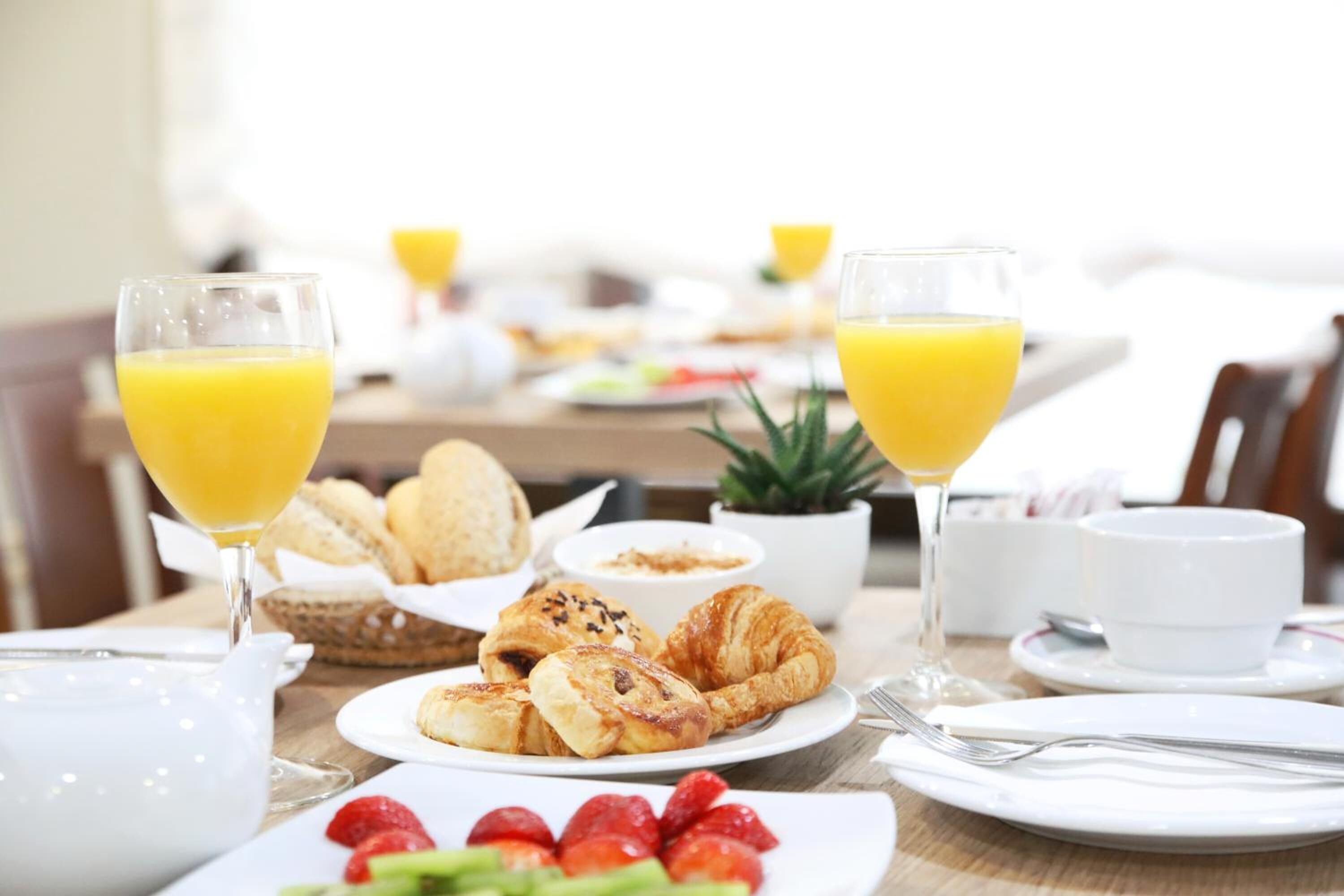 A breakfast setting with croissants, strawberries, and orange juice glasses on a table.