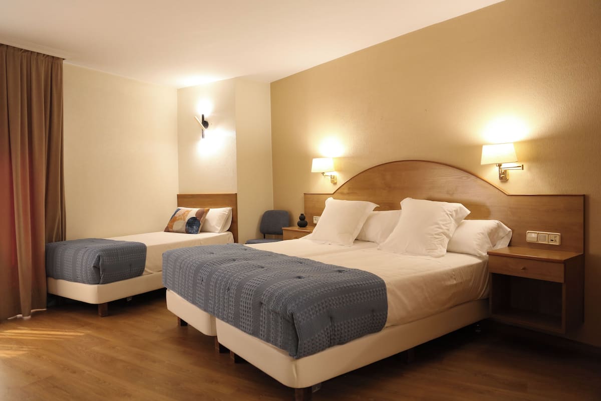 Habitación de hotel con dos camas, cabecero de madera, lámparas de noche y suelo de madera.