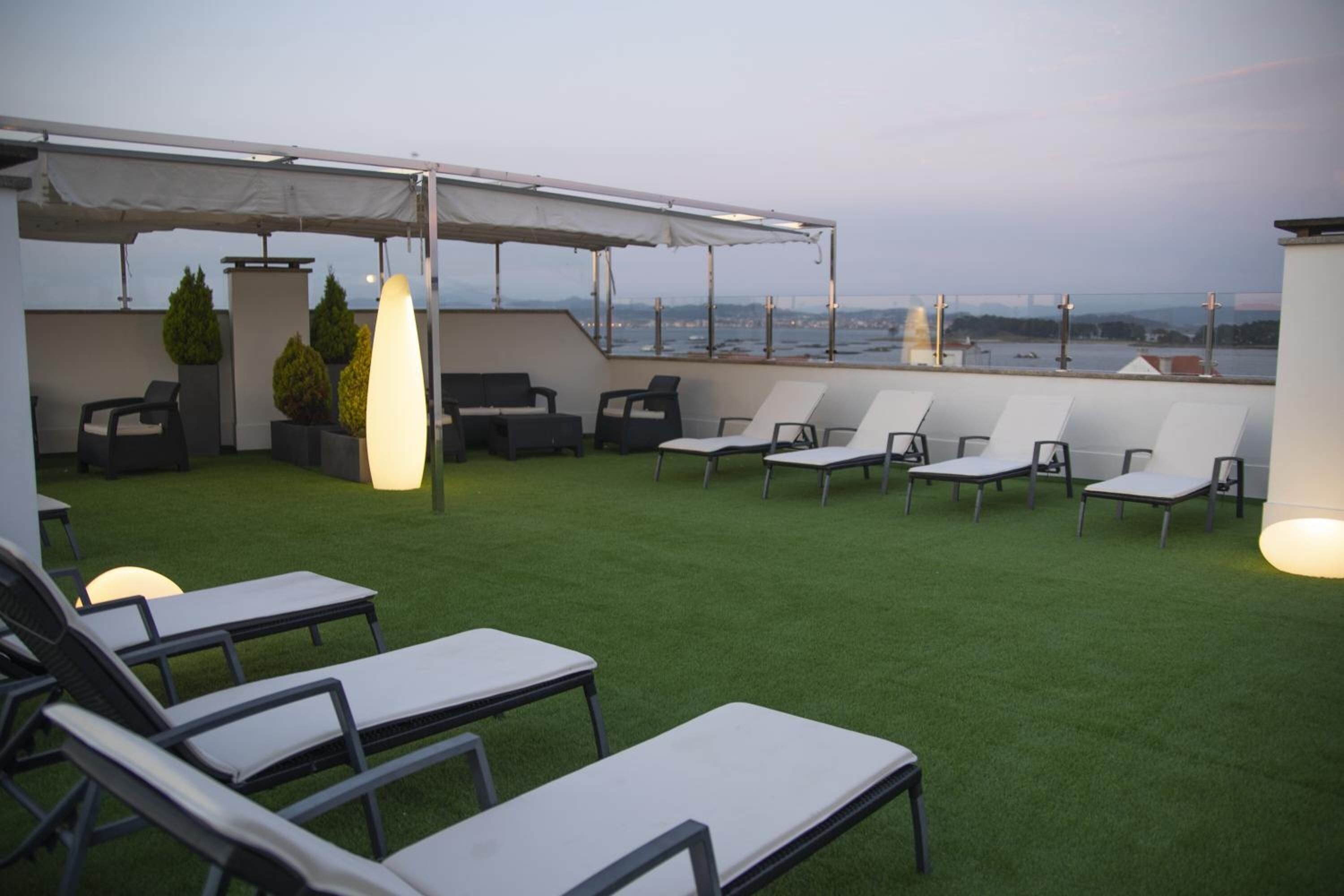 Een terras op het dak met lounge stoelen en een zonnescherm, met uitzicht op een stadsbeeld.