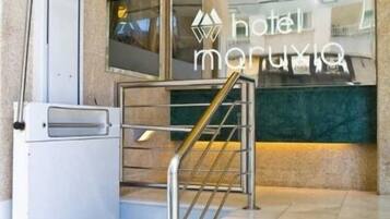 Entrada de hotel con rampa y escaleras, una recepción y un muro de mármol verde.