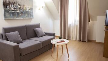 A modern living room with a grey sofa, a small round table with a book and a plant, and a painting of sailboats on the wall.