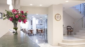 A hotel reception area with a marble counter, a vase of flowers, a sign indicating the hotel name, and a staircase leading to an upper level.