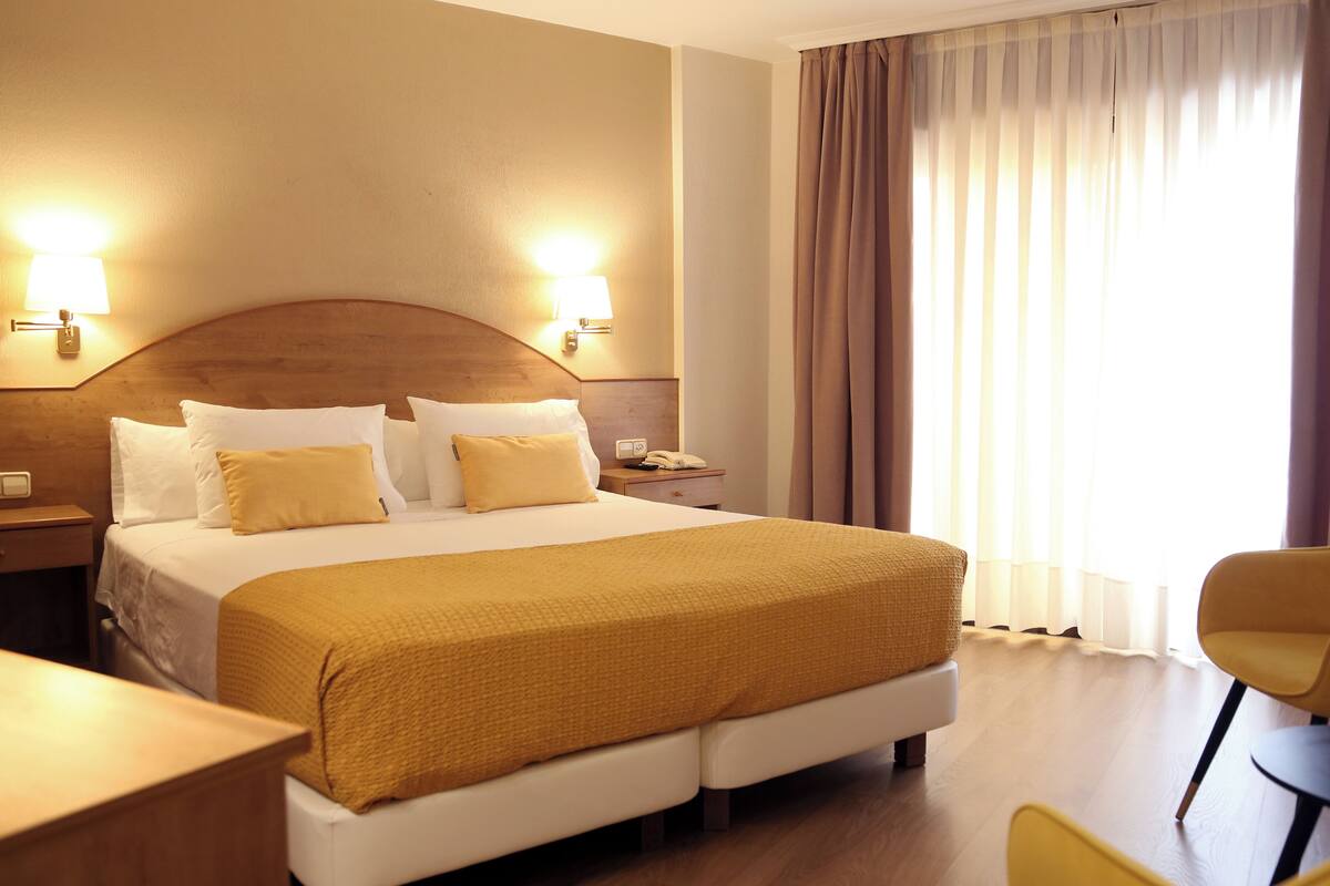 Una habitación de hotel con una cama grande, dos lámparas de noche, una mesita de noche y una silla.