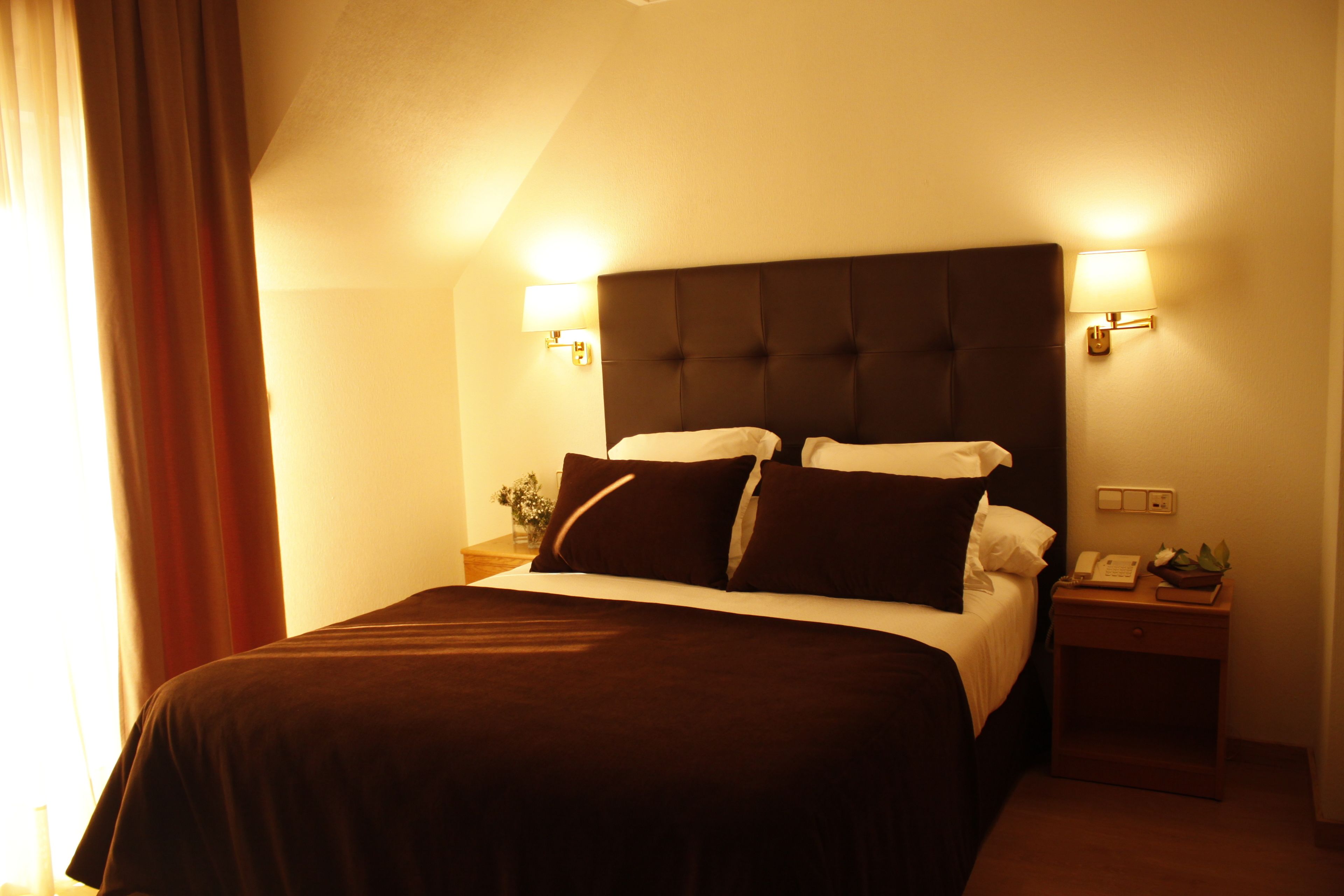 Una habitación de hotel con una cama grande, dos mesitas de noche y una lámpara.