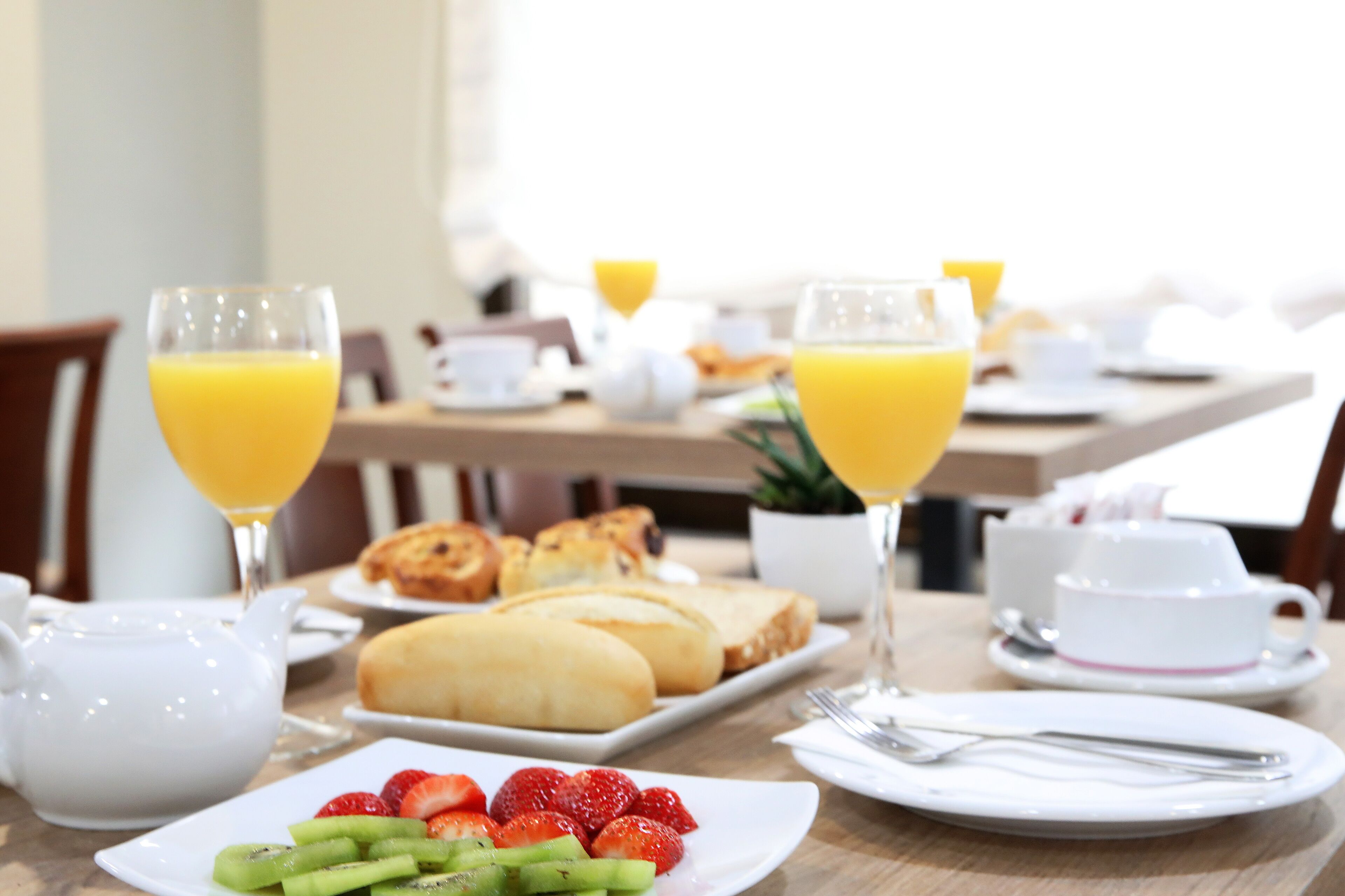 A breakfast table with plates of fruit, toast, croissants, and glasses of orange juice.