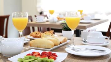 A breakfast table with plates of fruit, toast, croissants, and glasses of orange juice.