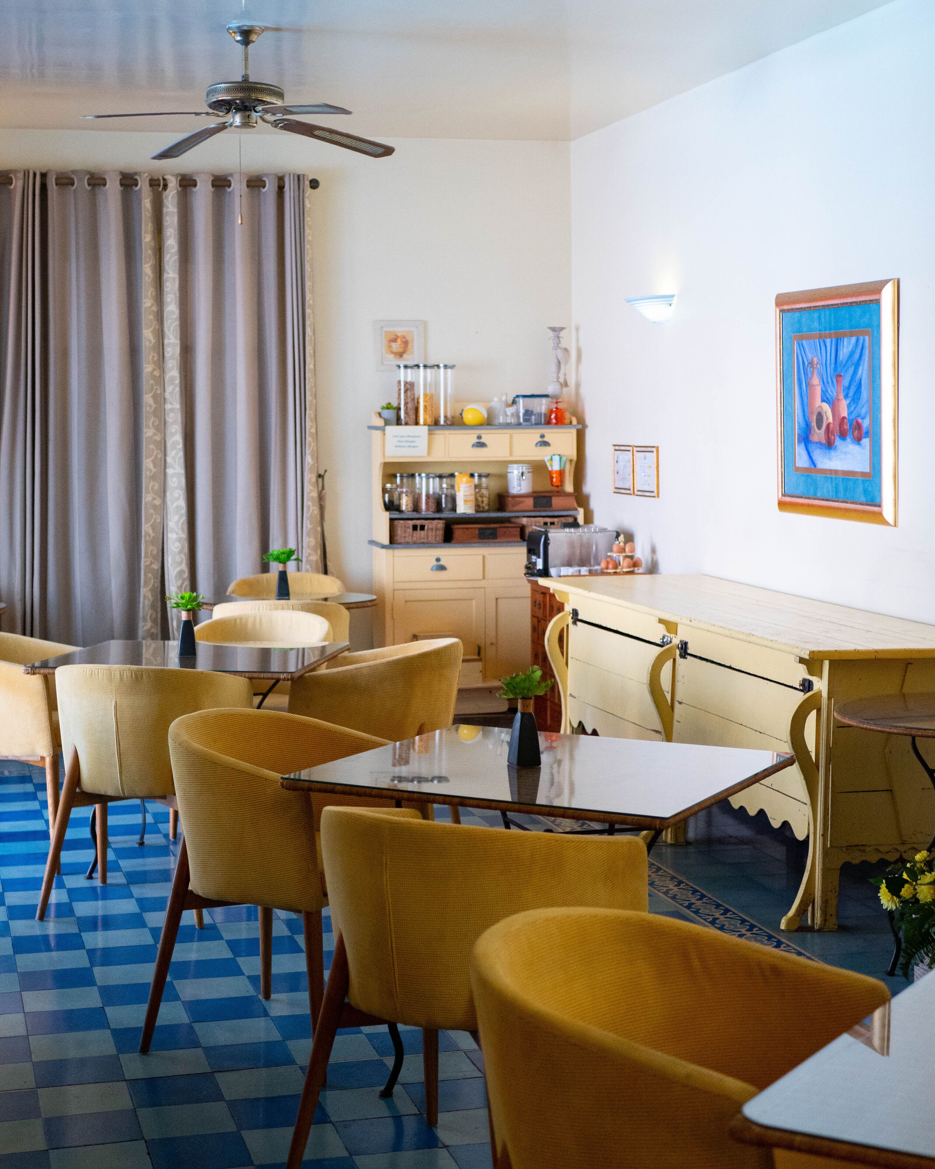 Uma sala de jantar com cadeiras amarelas e uma mesa, uma cozinha com armários e eletrodomésticos, e um ventilador de teto.
