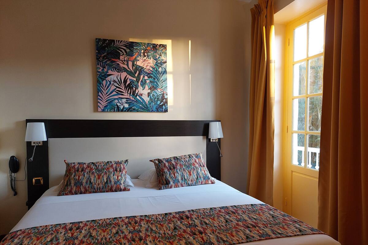 Une chambre d’hôtel avec un grand lit, deux lampes de chevet, un tableau au mur et une fenêtre avec des rideaux.