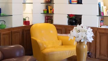 Een woonkamer met een gele fauteuil, een bruine leren bank, een salontafel en een boekenkast met diverse objecten.