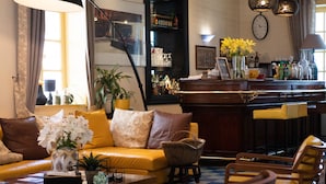 A cozy living area with a sofa, chairs, a coffee table, and a bar area with bottles and glasses. - Hotel le Juliette Dodu (Saint-Denis)