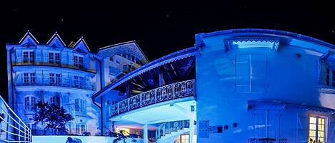 A large, multi-story building with a prominent balcony and a pool area.