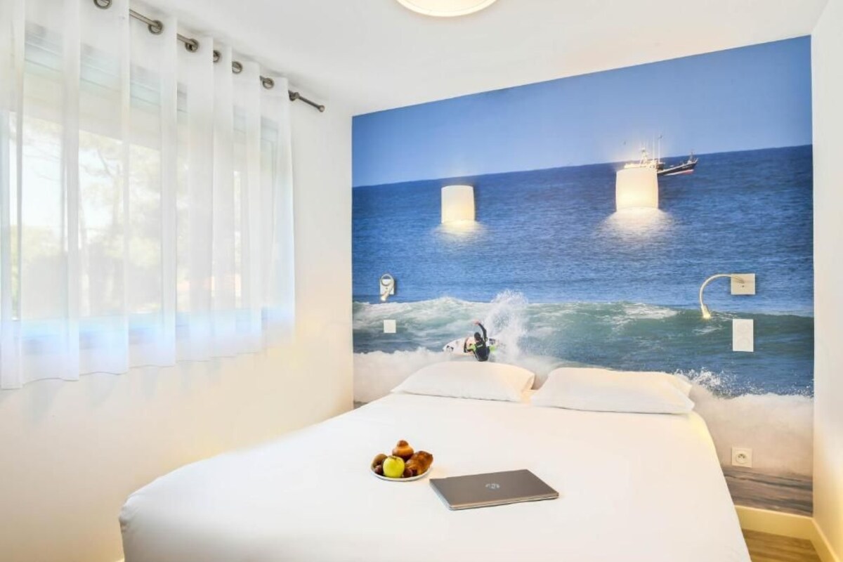 Quarto de hotel com uma cama, um laptop e uma tigela de frutas sobre a cama.
