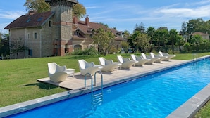 A swimming pool with lounge chairs and a stone building with a tower in the background. - Beaumanoir Small Luxury Boutique Hotel (Biarritz)