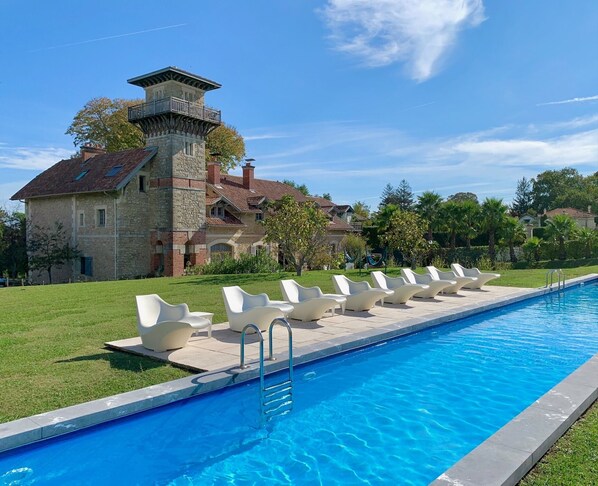 A swimming pool with lounge chairs and a stone building with a tower in the background.