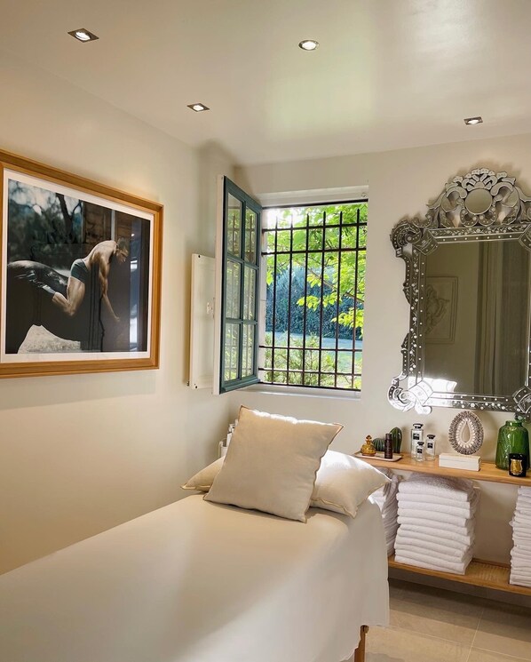 Un dormitorio con una cama, un espejo grande, una ventana con rejas e imagen enmarcada en la pared.