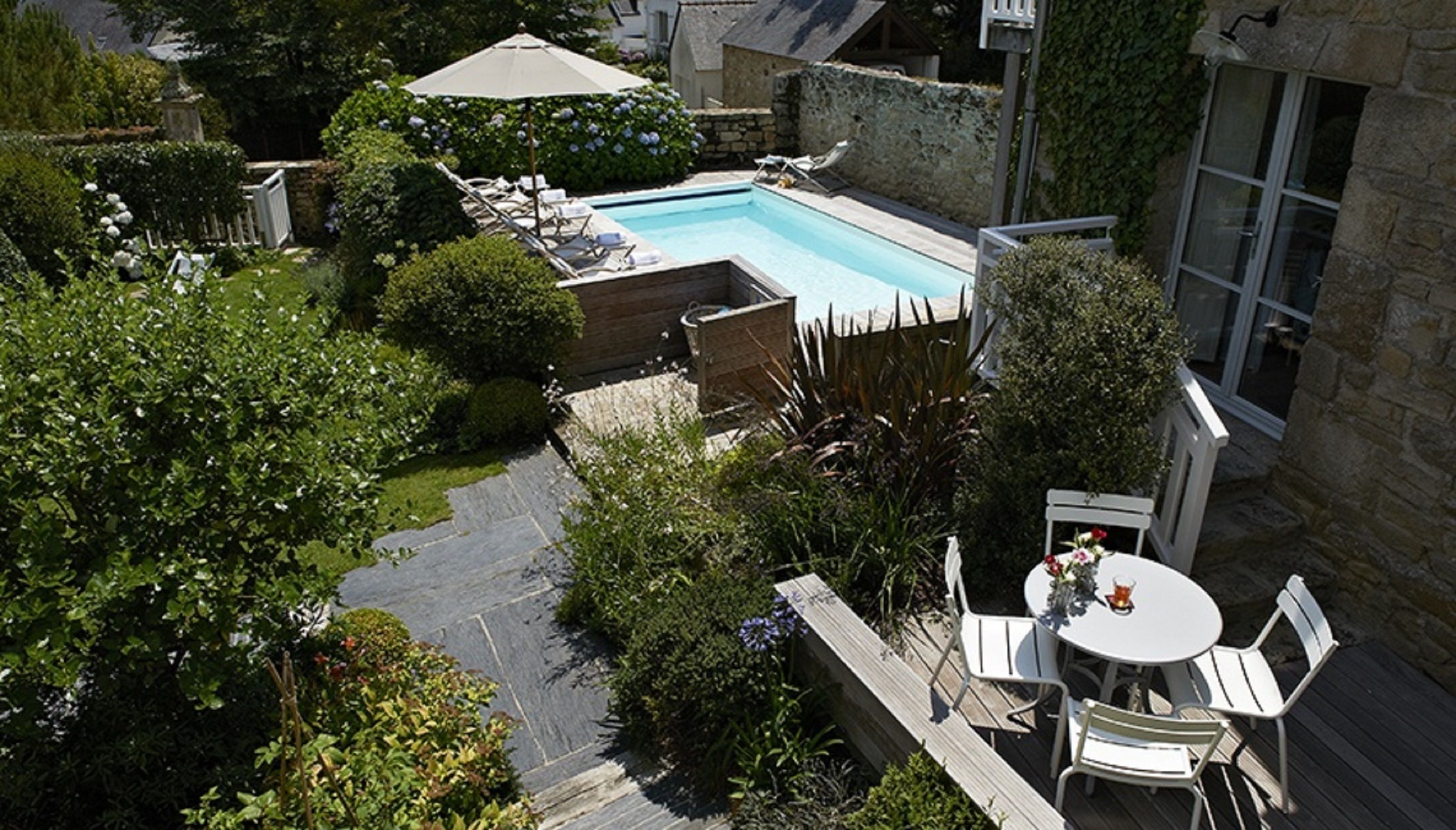 Una piscina en la azotea con sillones de descanso, rodeada de exuberante vegetación y muros de piedra.
