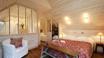 Un dormitorio acogedor con techo de madera, una cama grande con colcha floral roja, un sillón blanco y un banco de madera.