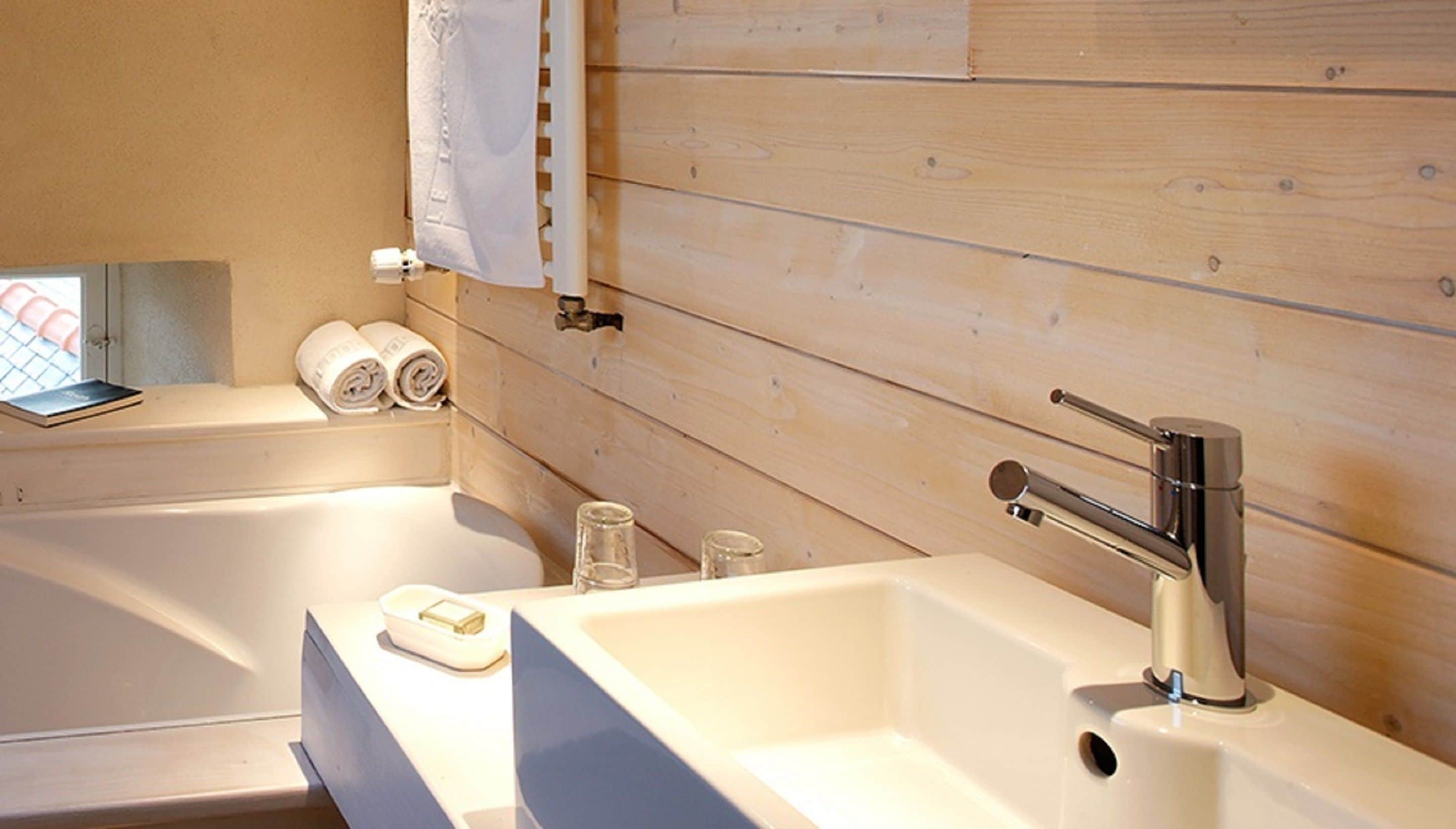 Un baño moderno con pared de madera, una bañera, un lavabo y dos toallas enrolladas.
