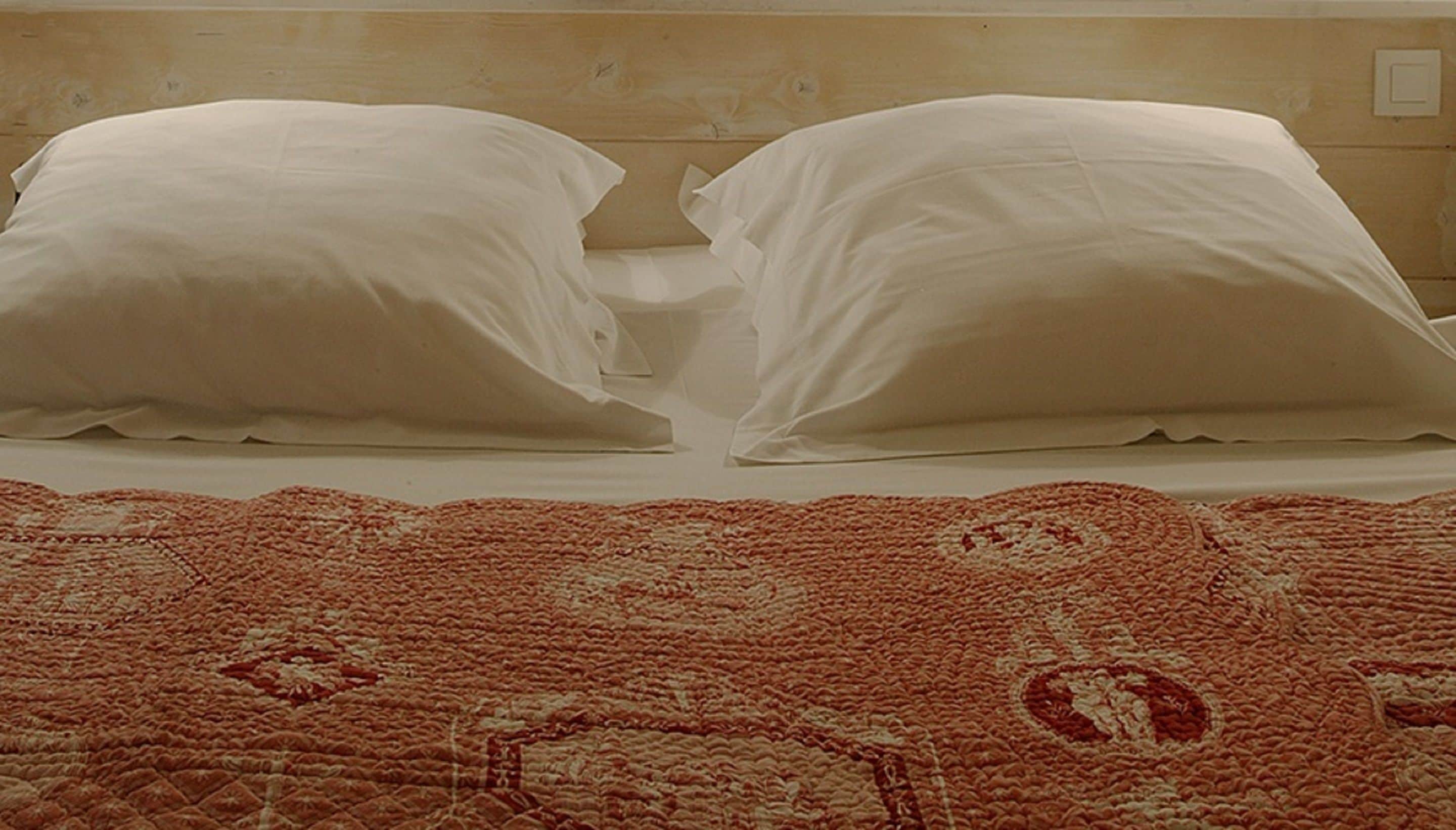 Una cama con almohadas blancas y una colcha estampada roja.