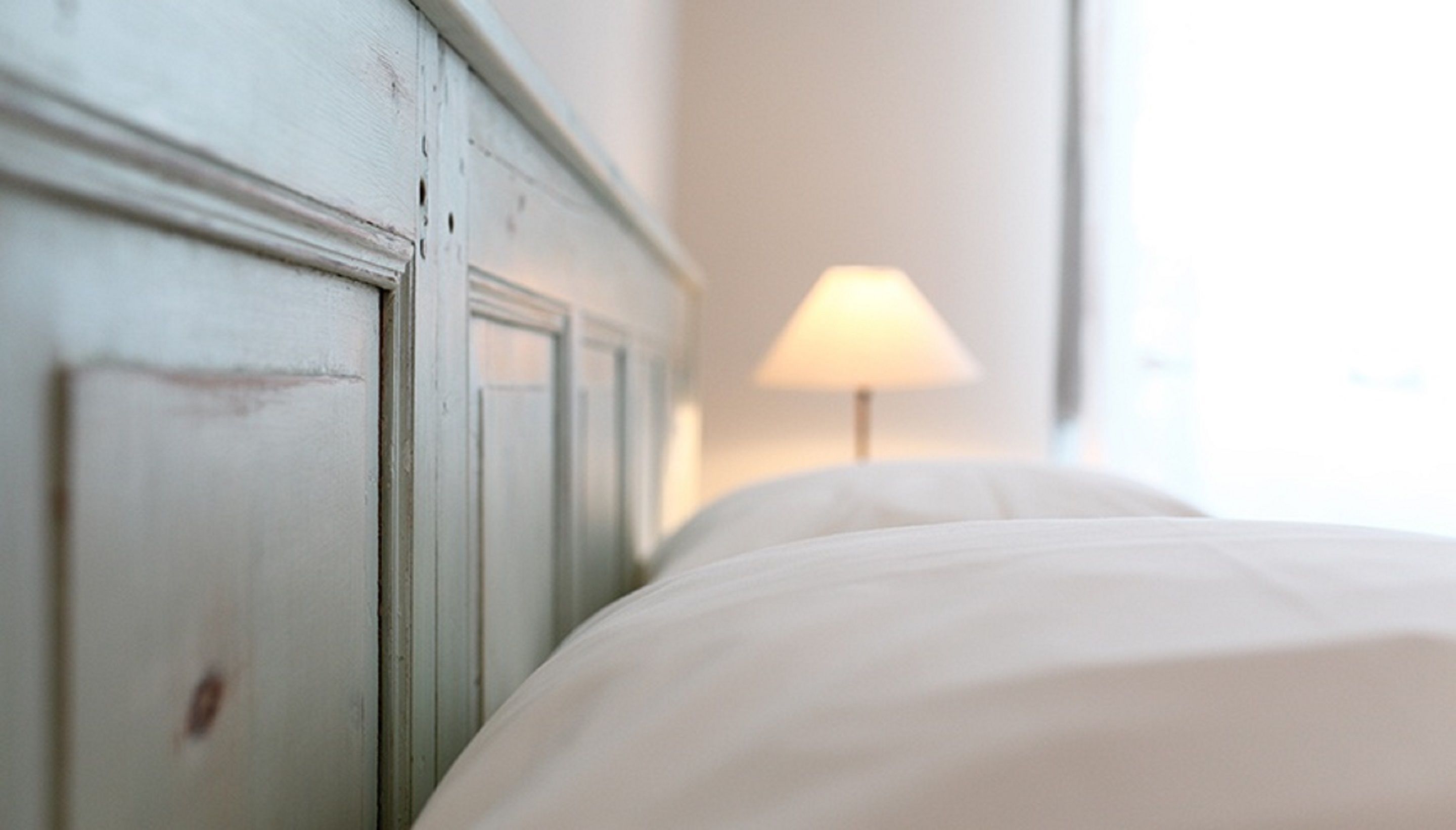 A bed with white linens and a wooden headboard.