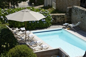 A swimming pool with lounge chairs and an umbrella, surrounded by greenery and stone walls. - Le Lodge Kerisper (La Trinite-sur-Mer)
