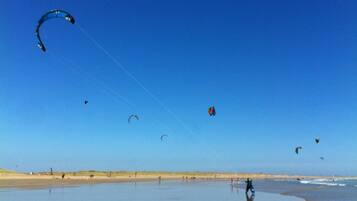 Una playa con gente volando cometas y parapentes.