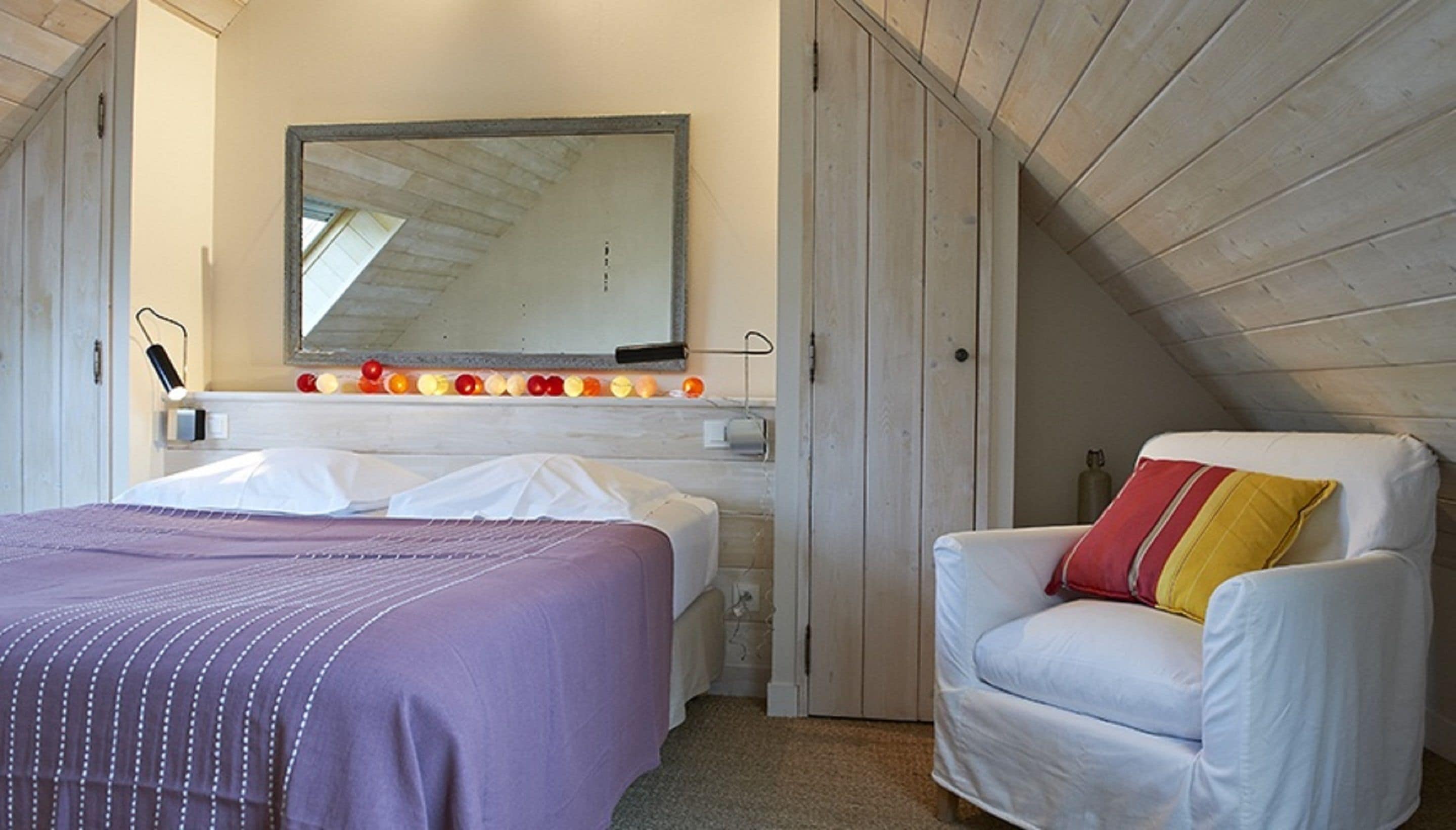 Un dormitorio con cama, una silla, un espejo y una estantería con adornos.